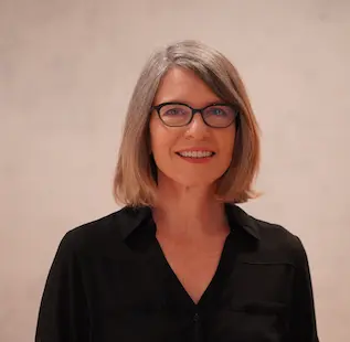Woman with shoulder-length gray hair and glasses, smiling at the camera, wearing a black blouse.